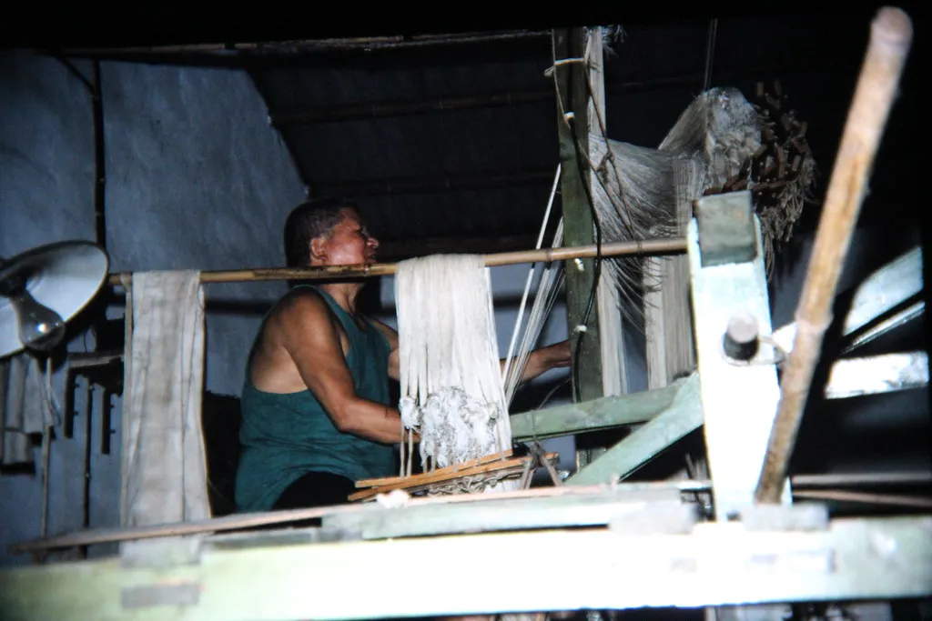 Weaver working at a wooden frame loom with warp threads hanging
